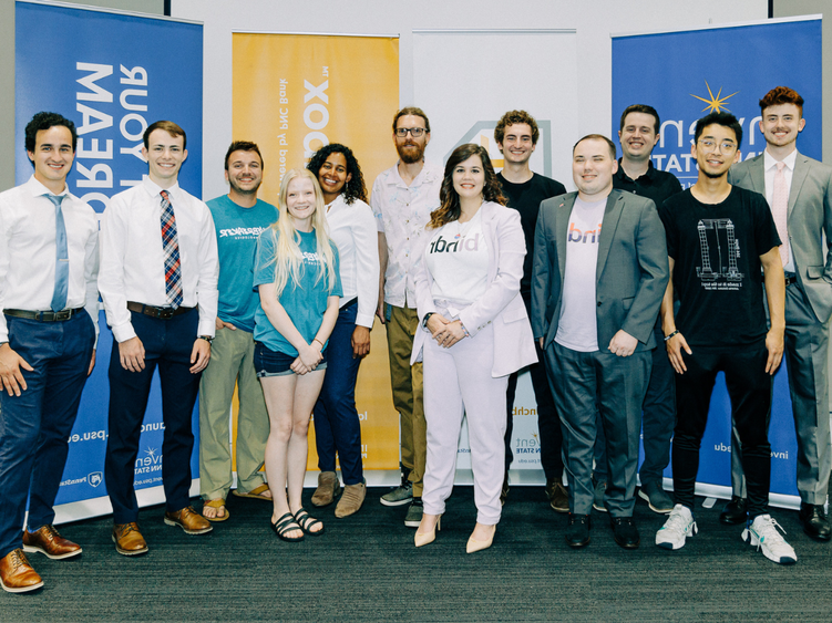 12 students pose standing for photo in front of Invent Penn State signage